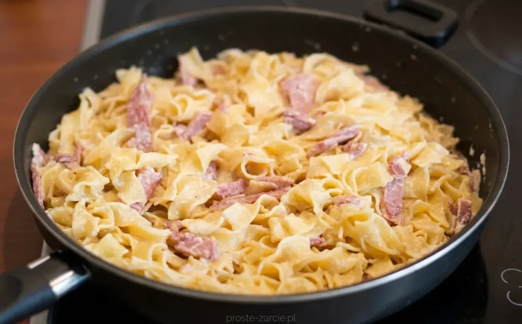 Kremowy makaron tagliatelle w sosie śmietanowym z paskami podsmażonej szynki, posypany żółtym serem.