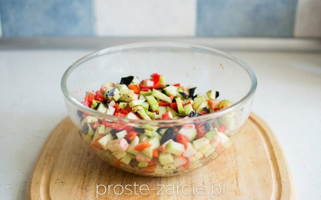 Szklana miska z kolorową sałatką z surimi, zielonym awokado, czerwoną papryką i kawałkami ciemnych glonów nori.