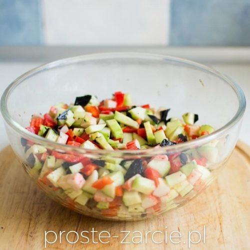 Szklana miska z kolorową sałatką z surimi, zielonym awokado, czerwoną papryką i kawałkami ciemnych glonów nori.