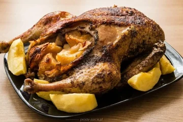 Rumiana, upieczona kaczka nadziewana jabłkami, podana na półmisku w otoczeniu pieczonych ćwiartek owoców.