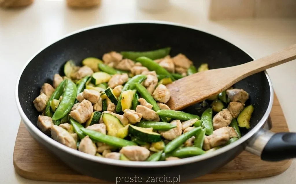 Kremowy makaron spaghetti z zielonymi strączkami groszku cukrowego, kawałkami kurczaka i cukinii, posypany świeżo mielonym pieprzem.