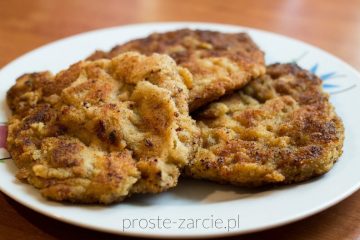 Złocisty, chrupiący kotlet schabowy podany z ziemniakami i koperkiem na białym talerzu.