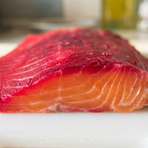 Cienkie plastry różowego łososia gravlax z rubinową obwódką z buraków, podawane na desce, proste żarcie