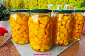 Słoiki z jasno-pomarańczową dynią w occie, wewnątrz widoczne goździki i laska cynamonu w klarownej zalewie.
