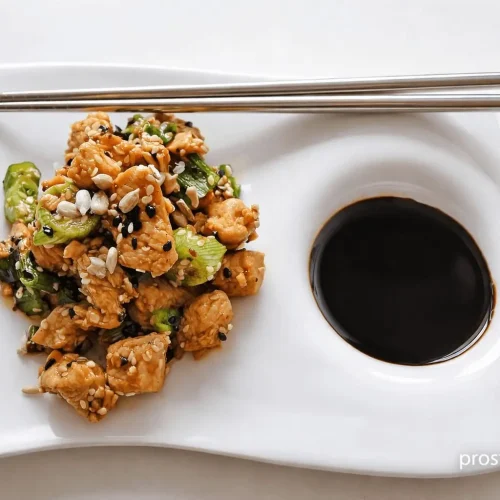 Kawałki indyka w ciemnym sosie teriyaki posypane sezamem podane z ryżem