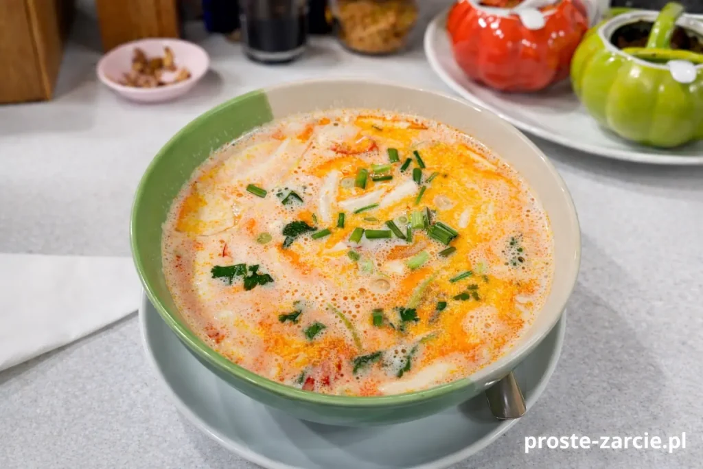Kremowa, pomarańczowa zupa tajska Tom Yum z mleczkiem kokosowym i owocami morza, podana w zielonej misce.