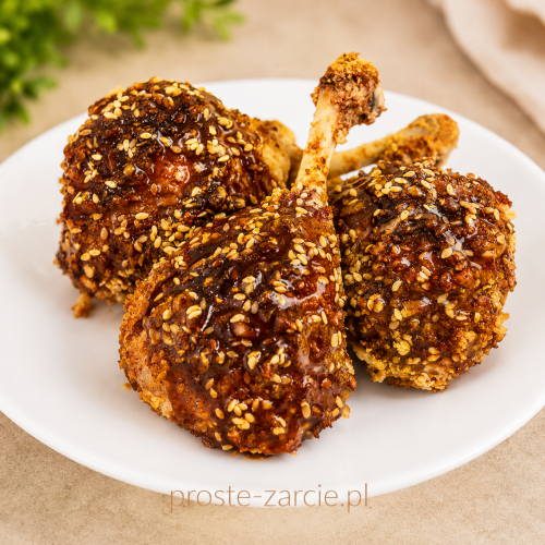Kawałki chrupiącego koreańskiego kurczaka w lepkim czerwonym sosie gochujang posypane szczypiorkiem i sezamem.