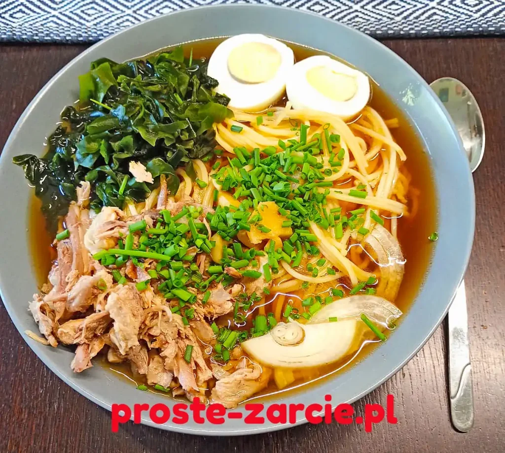 Głęboka miska z ramenem z pieczonej kaczki, makaronem udon, jajkiem na twardo, glonami wakame i szczypiorkiem.