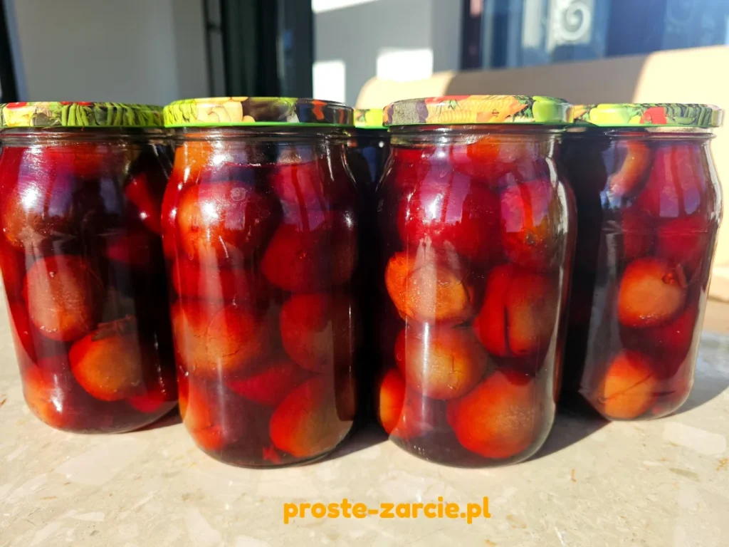 Gorący słoik wypełniony po szczyt jędrnymi śliwkami w occie z goździkami, stojący na marmurowym stole.