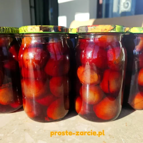 Gorący słoik wypełniony po szczyt jędrnymi śliwkami w occie z goździkami, stojący na marmurowym stole.