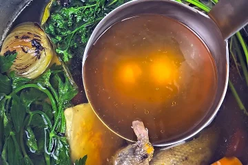 Talerz klarownego rosołu z gołębia serwowany z makaronem krajanka i świeżą natką pietruszki.