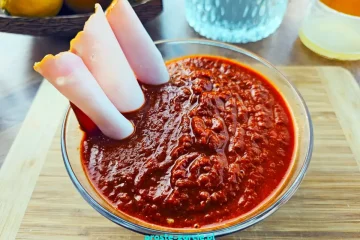 Gładki, ciemnobordowy domowy sos barbecue w małej miseczce obok słoiczka i składników.