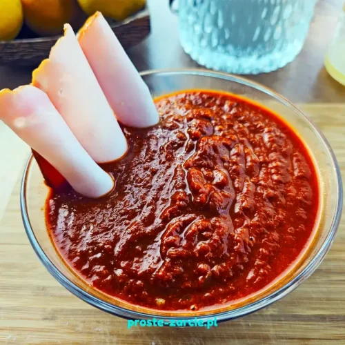 Gładki, ciemnobordowy domowy sos barbecue w małej miseczce obok słoiczka i składników.